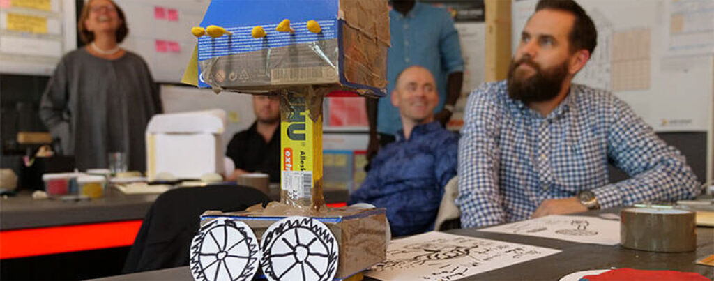 Workshop-Team präsentiert schnellen Prototyp aus Papier und Kleber als Symbol für Design Thinking - TOM SPIKE Structured innovation