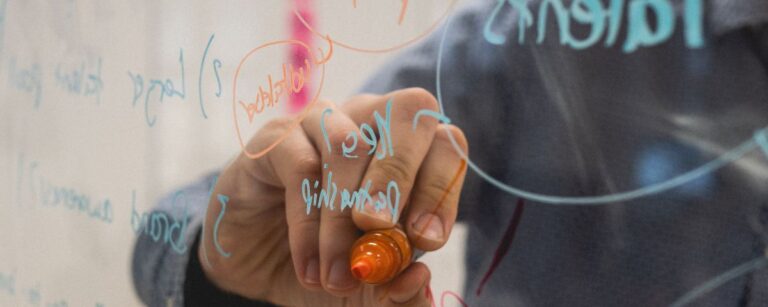Hand mit Marker schreibt auf Glas als Symbol für Ideenentwicklung im B2B-Unternehmen - TOM SPIKE