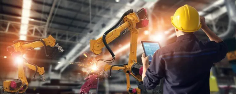 Schweißroboter und Mitarbeiter mit Helm und Tablet als Symbol für Geschäftsmodellinnovation in Industrieunternehmen - TOM SPIKE